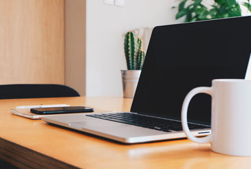 Laptop domputer on a desk next to a coffee cup