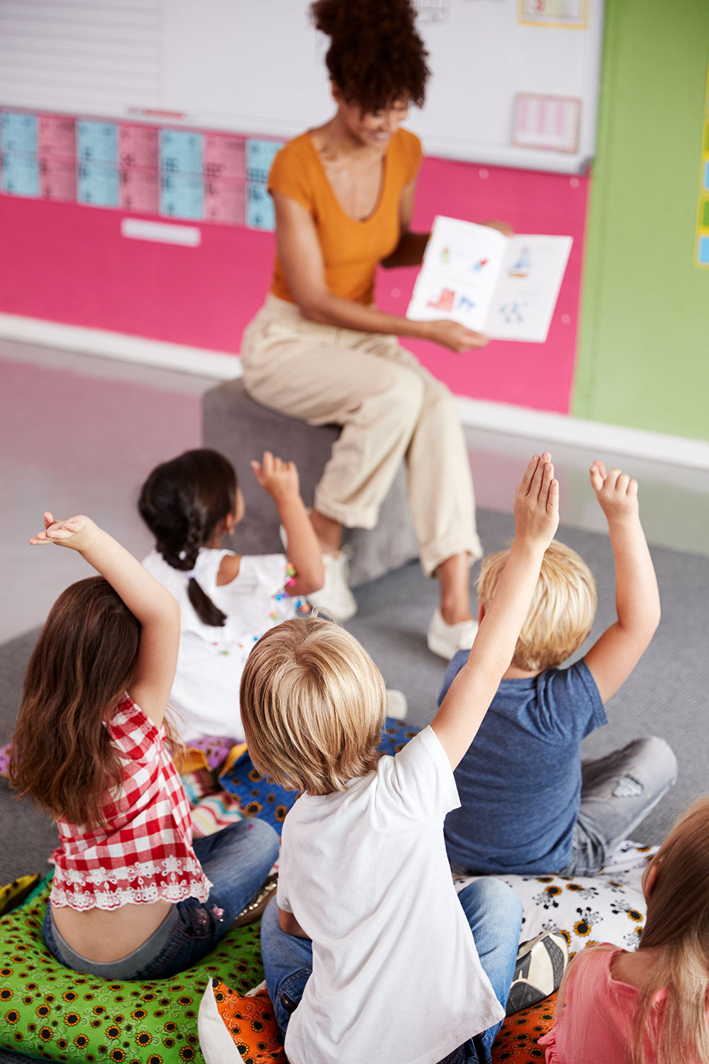 Classroom of students and teacher raising hands.